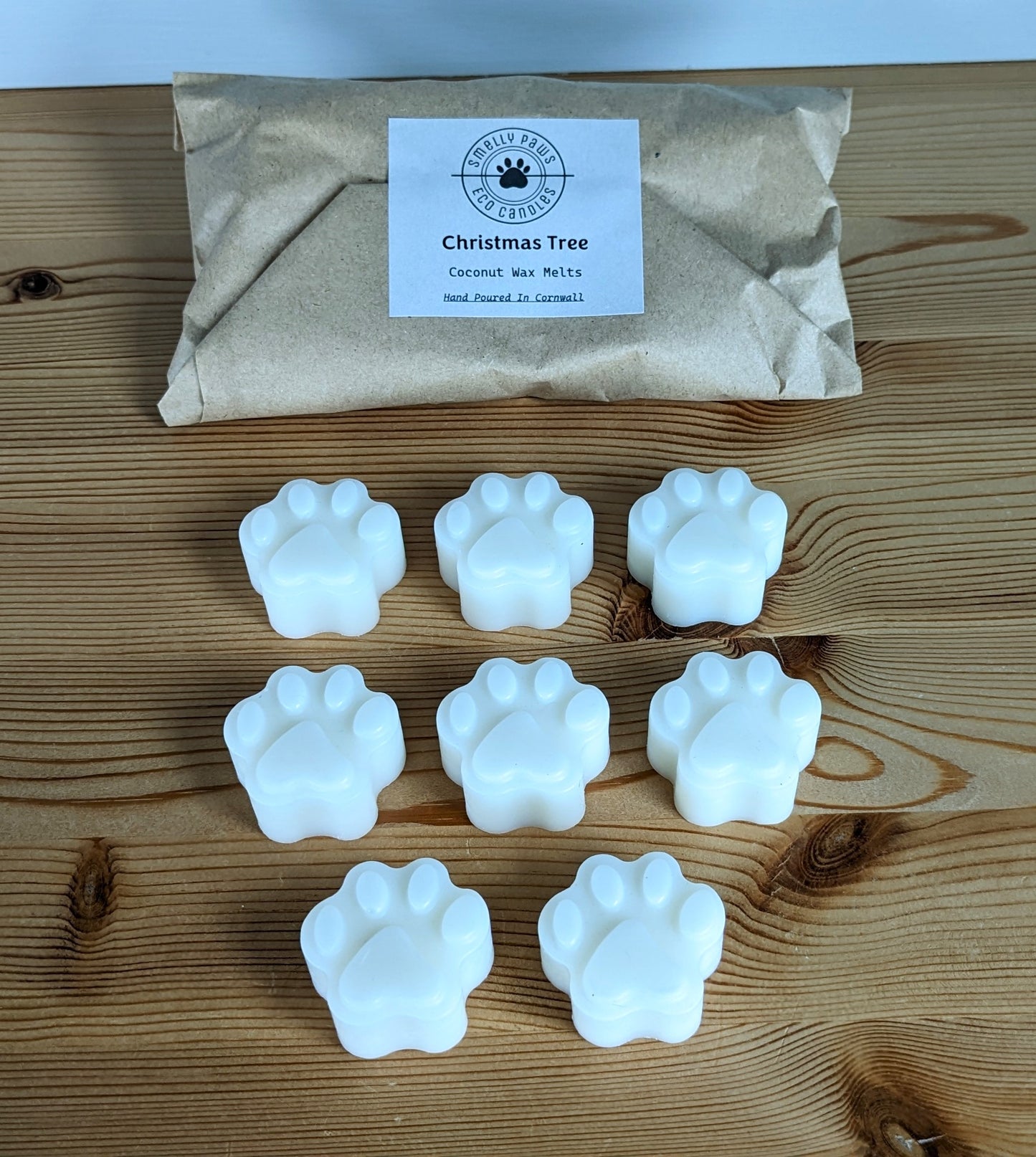 8 paw print wax melts sat on a wooden counter with brown paper packaging bag behind
