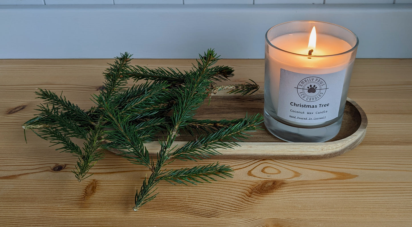 Burning Christmas tree candle sat on a wooden tray with sprigs of fresh Christmas tree