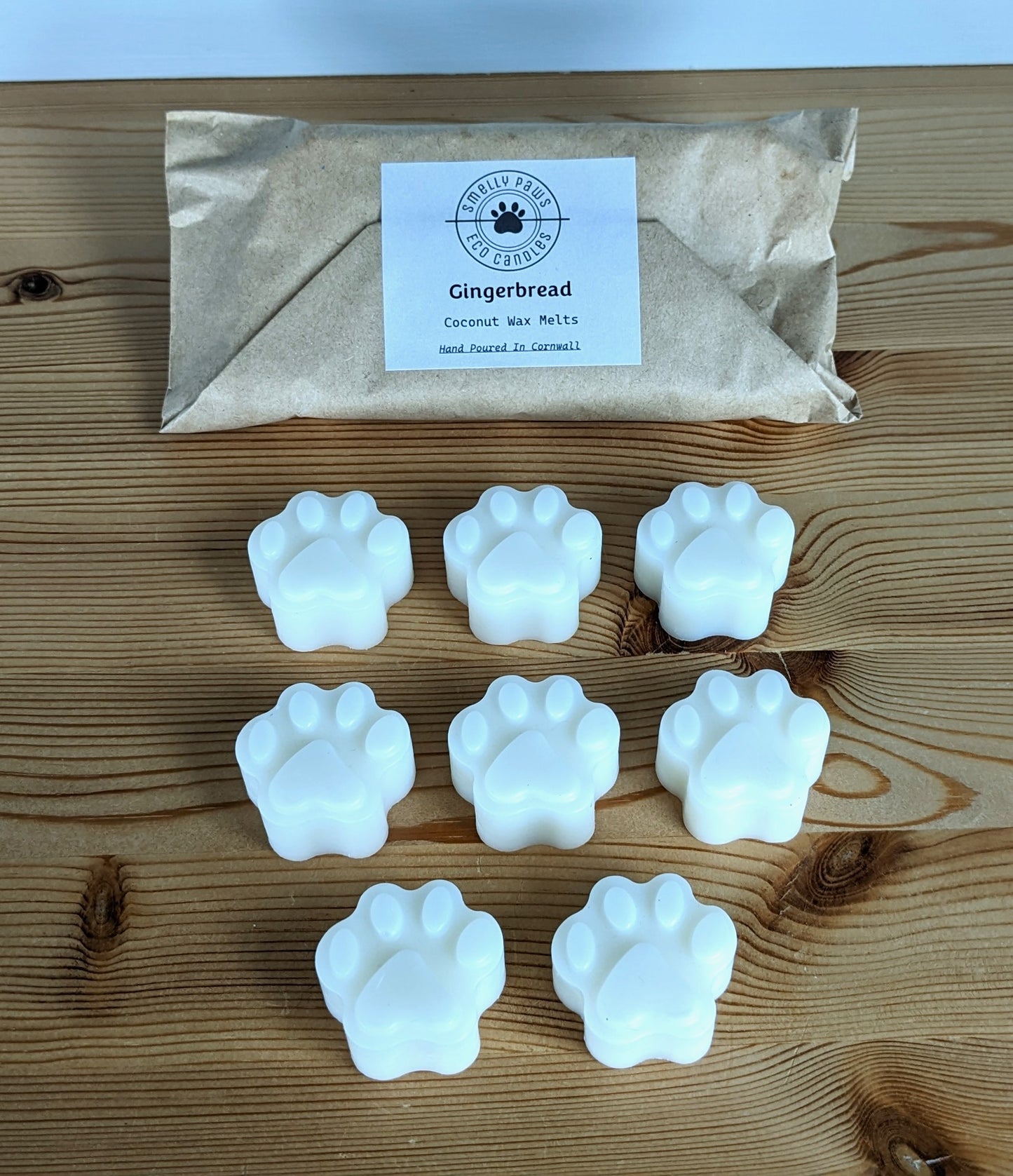 8 paw print wax melts sat on a wooden counter with brown paper packaging bag behind