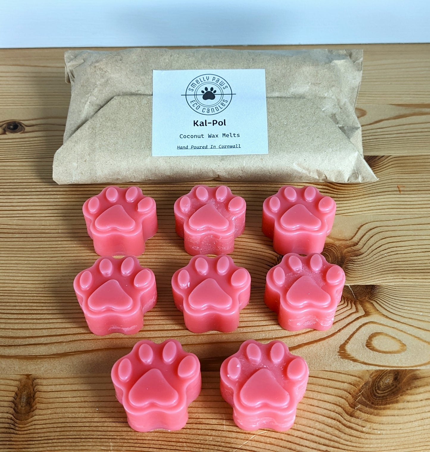 8 pink coloured paw print wax melts sat on a wooden counter with brown paper packing bag behind