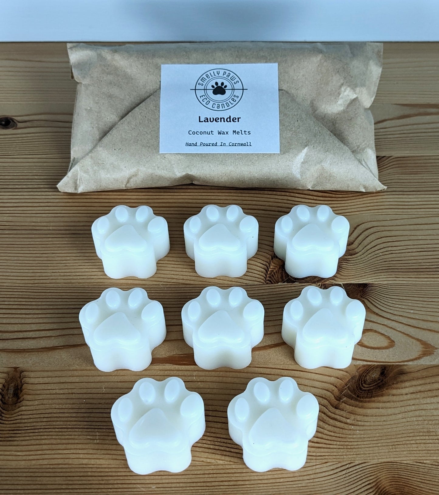 8 paw print wax melts sat on a wooden counter with brown paper packaging bag behind