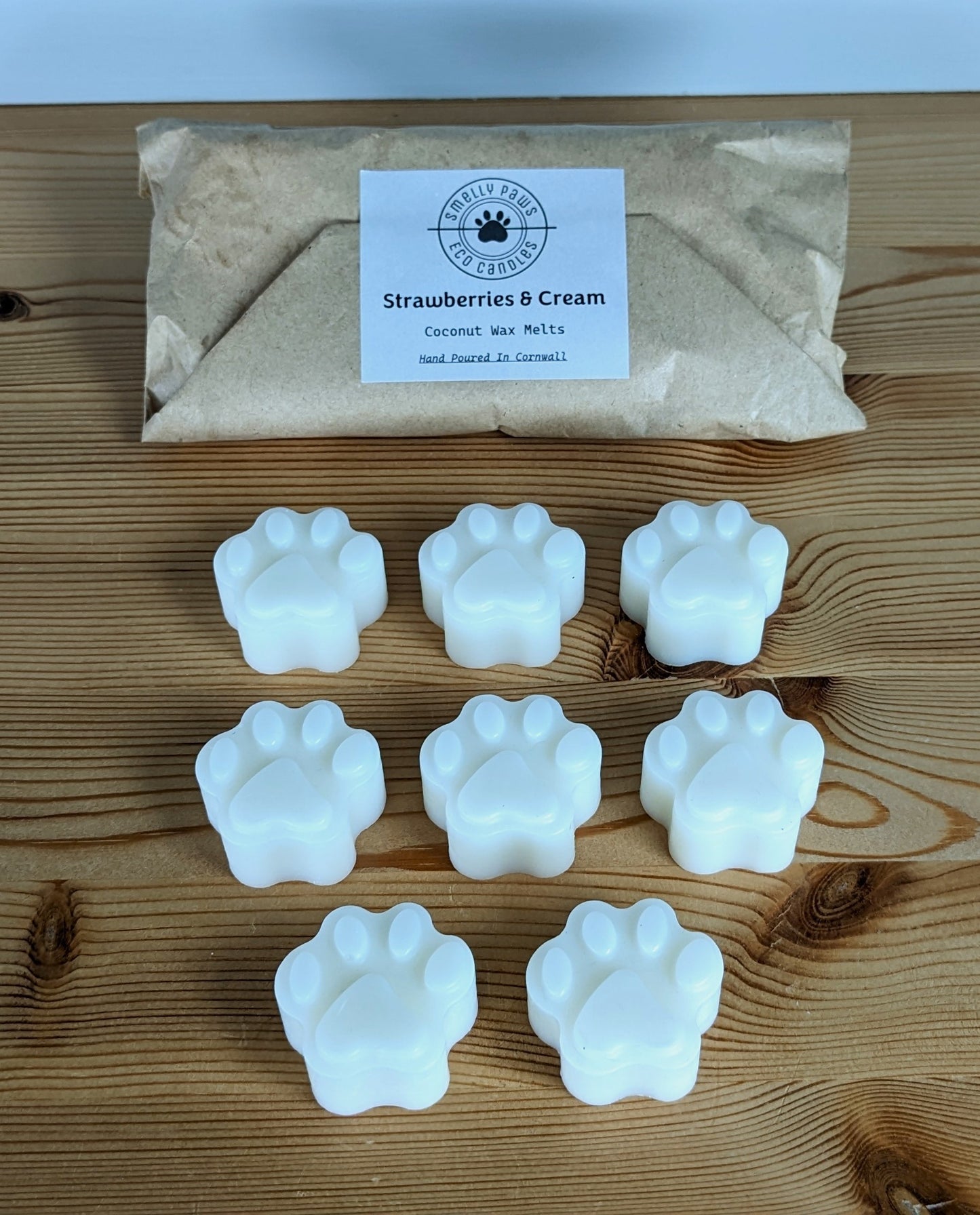8 paw print wax melts sat on a wooden counter with brown paper packaging bag behind