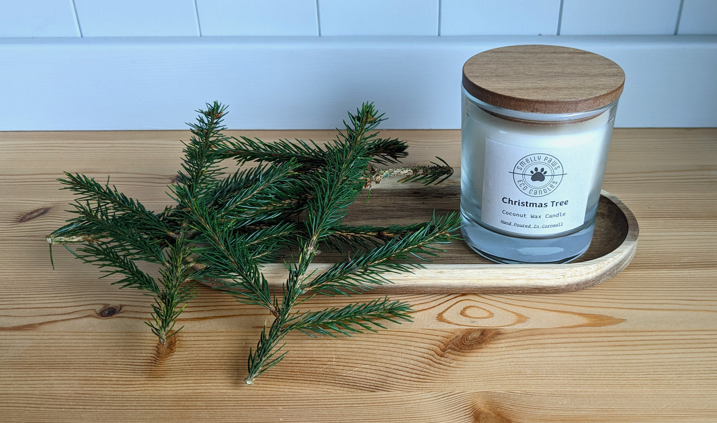 Christmas tree candle with wooden lid sat on a wooden tray with sprigs of fresh Christmas tree 
